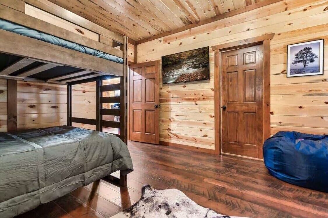 Interno di una baita con un letto a castello, pareti in legno, un quadro e una porta.