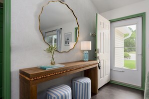 A hallway with a wooden console table, a mirror, a lamp, and two striped ottomans. - Coastal 3BR Retreat with Firepit & Hot Tub in Wilmington NC (Wilmington)