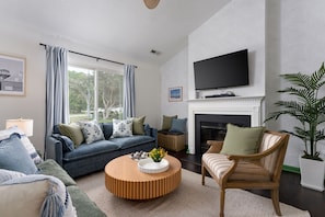 Een woonkamer met een bank, fauteuil, rond bijzettafeltje en een open haard.
