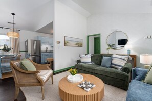 Een moderne woonkamer met een bank, stoelen, een salontafel en een keuken met een koelkast.