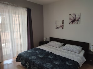 A bedroom with a bed, a nightstand, a lamp, and a window with curtains. - Your Perfect Summer Getaway in Croatia (Krk)