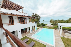 A two-story building with a swimming pool, a covered patio, and a view of the ocean.