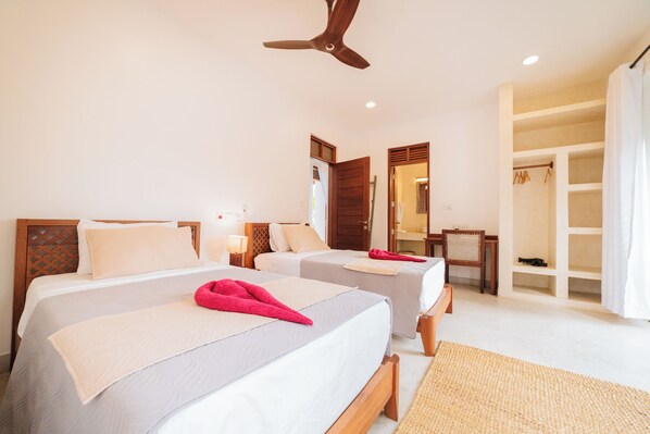 Una habitación de hotel con dos camas, ventilador de techo, espejo y vestidor.