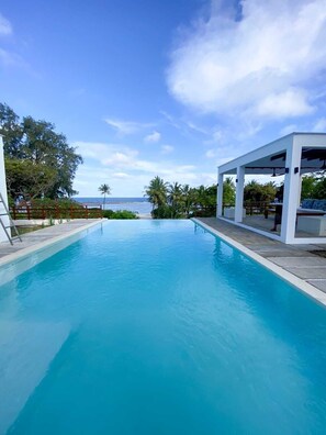 Una piscina azul cristalina con vista al océano, rodeada por una estructura blanca con techo.