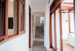 A hallway with wooden doors and windows, a staircase leading to an upper floor, and a patterned rug on the floor.