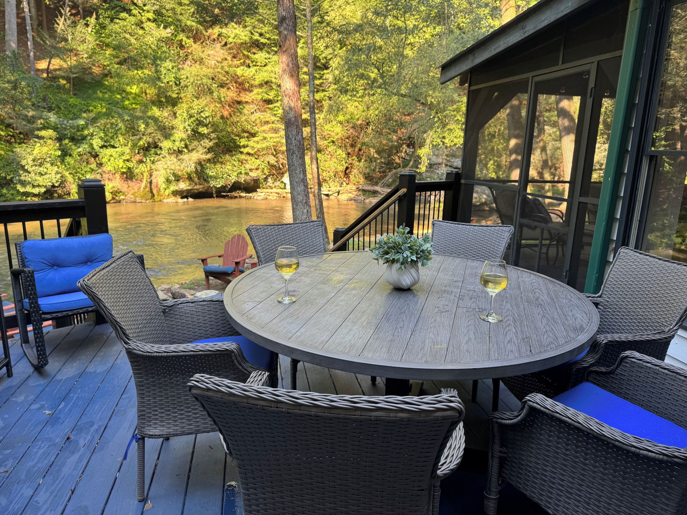 A deck with wicker furniture, two glasses of wine, and a potted plant.