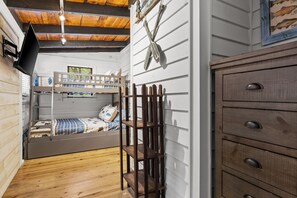 Quarto compacto com beliche, prateleiras de madeira, cômoda e um quadro de peixes fixado na parede.