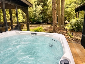Ein Whirlpool in einem überdachten Außenbereich mit Holzterrasse, umgeben von Bäumen und einer natürlichen Landschaft.