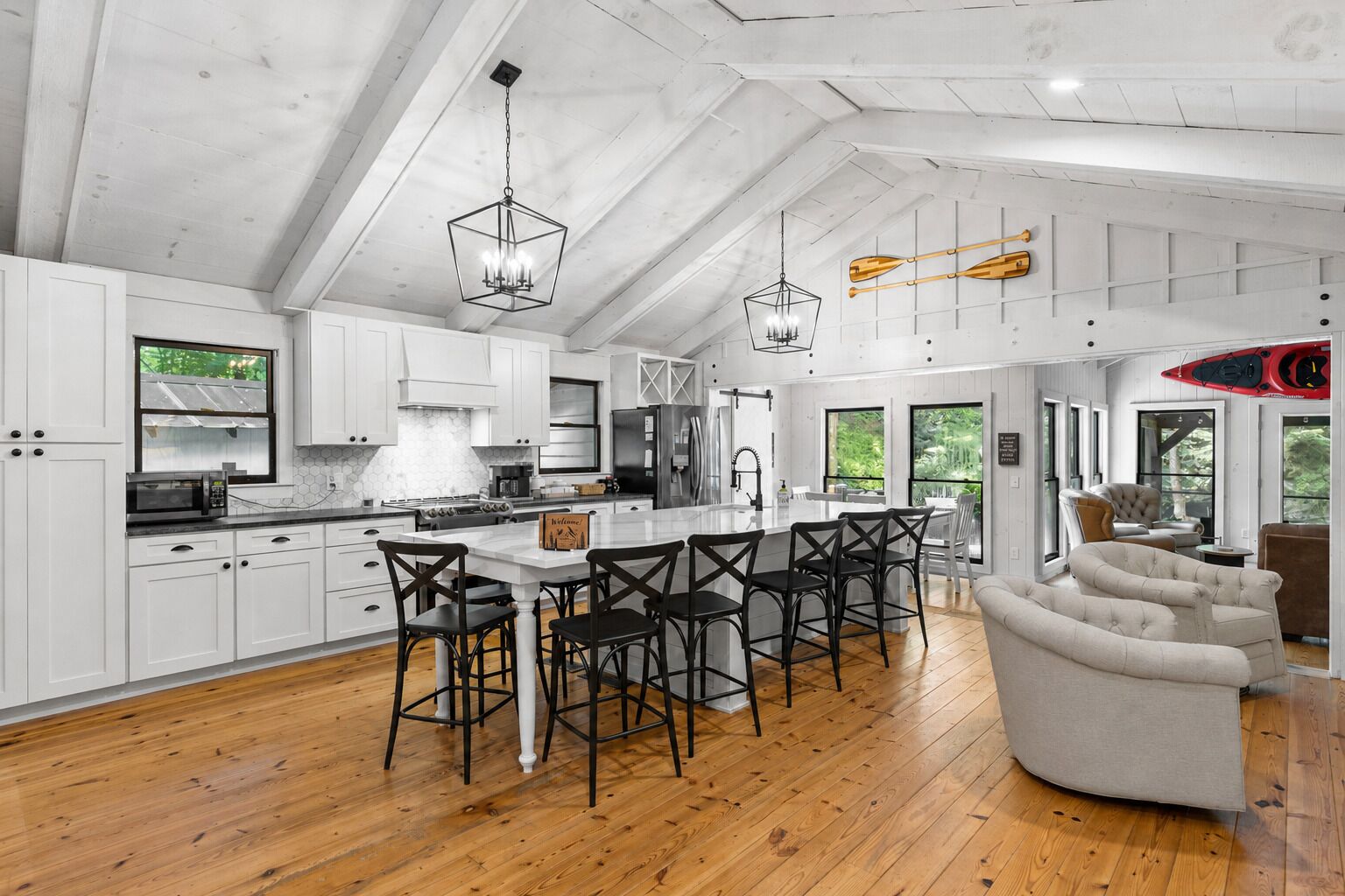 A modern kitchen with white cabinets, a central island with bar stools, and wooden flooring.