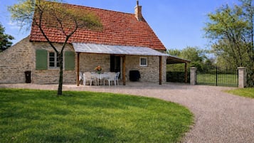 A stone house with a red-tiled roof, a gravel driveway, and a fenced garden area.