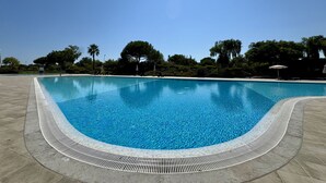 A clear blue pool with a tiled edge, surrounded by a paved area and trees. - Vilamoura Prestige 3 With Pool by Homing (Loulé)