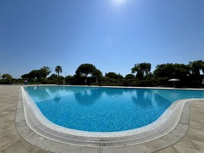A clear blue pool with a tiled edge, surrounded by a paved area and trees. - Vilamoura Prestige 3 With Pool by Homing (Loulé)
