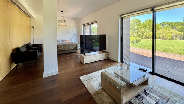 A modern living room with a large TV, wooden flooring, and a view of a green landscape through large windows. - Vilamoura Prestige 3 With Pool by Homing (Loulé)