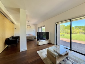 A modern living room with a large TV, wooden flooring, and a view of a green landscape through large windows. - Vilamoura Prestige 3 With Pool by Homing (Loulé)