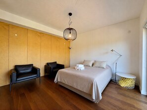 A modern bedroom with a large bed, two black chairs, a floor lamp, and a unique hanging light fixture. - Vilamoura Prestige 3 With Pool by Homing (Loulé)