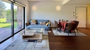 Ett modernt vardagsrum med en skjutdörr i glas som leder ut till en uteplats, en blå soffa med mönstrade kuddar, ett soffbord i glas och en matplats med en röd duk.