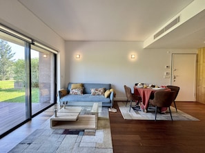 A modern living room with a glass sliding door leading to a patio, a blue sofa with patterned cushions, a glass coffee table, and a dining area with a red tablecloth. - VILAMOURA PRESTIGE 3 WITH POOL by HOMING (Vilamoura)
