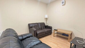 Um quarto com um sofá de couro preto, um sofá de couro marrom, uma mesa de centro de madeira e um abajur.
