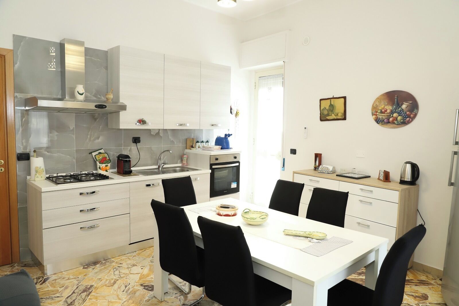 Una cocina compacta con estufa a gas, lavamanos y horno, una mesa de comedor con sillas y un refrigerador pequeño.