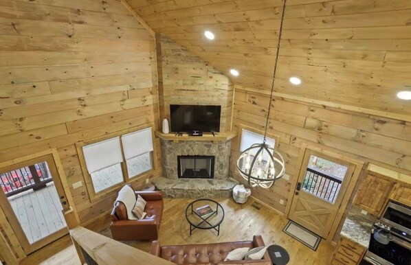 A wooden cabin interior with a stone fireplace, a television, and a dining area.