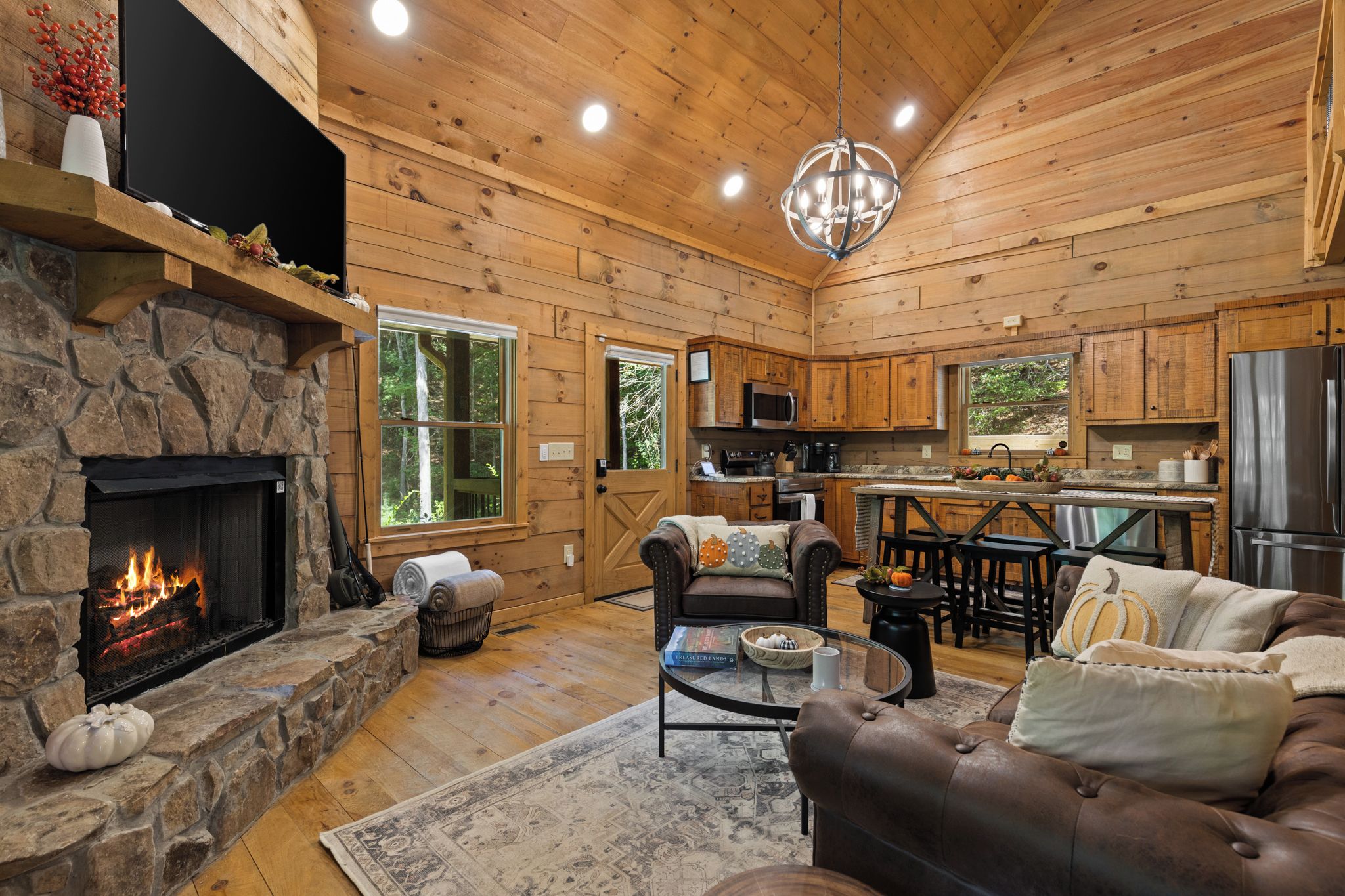 Interior acogedor de una cabaña con chimenea de piedra, sofá de cuero y una zona de cocina.