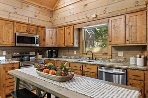 Une cuisine avec des meubles en bois, un four à micro-ondes, une cuisinière, un évier et une fenêtre donnant sur des arbres.
