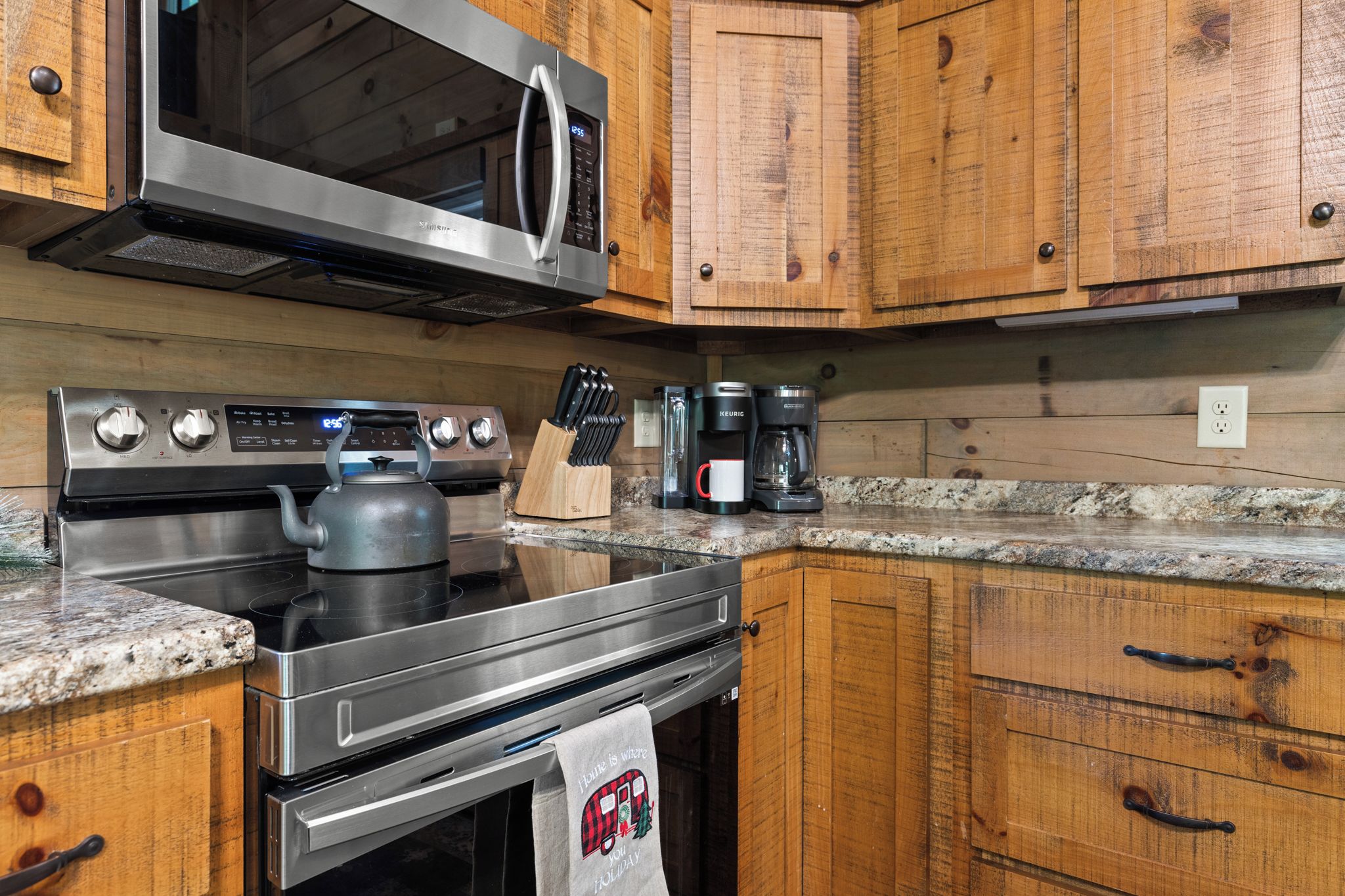 Una cocina con armarios de madera, electrodomésticos de acero inoxidable, una tetera, una cafetera y un bloque de cuchillos.