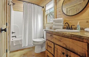 A bathroom with a shower, toilet, and wooden vanity with a sink and mirror.