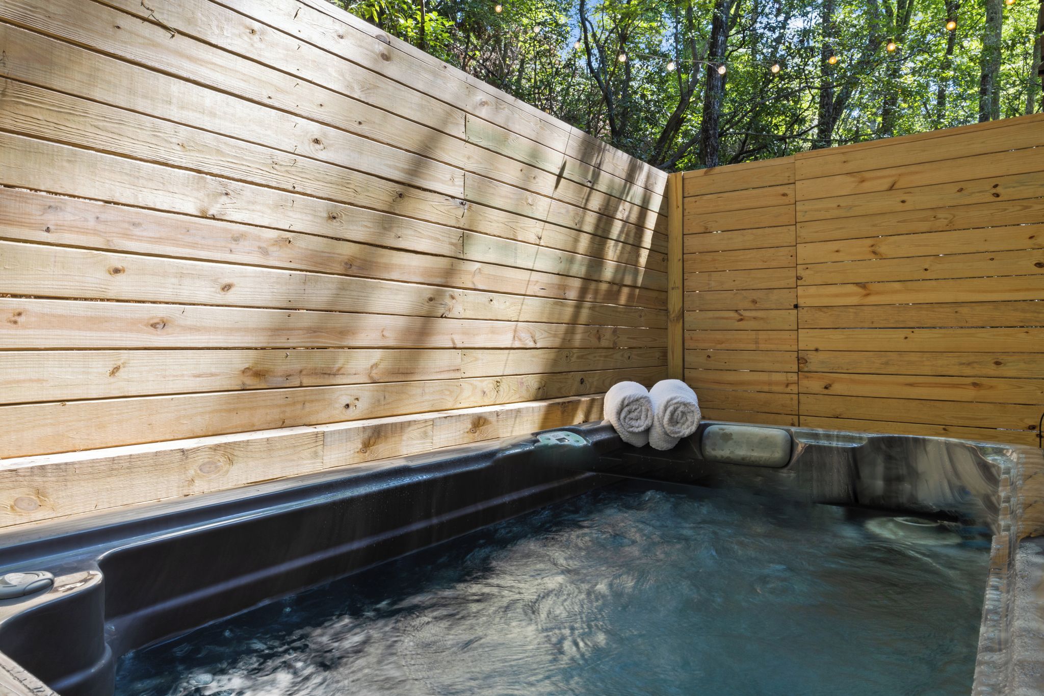 A hot tub with wooden walls and a metal frame, surrounded by trees.