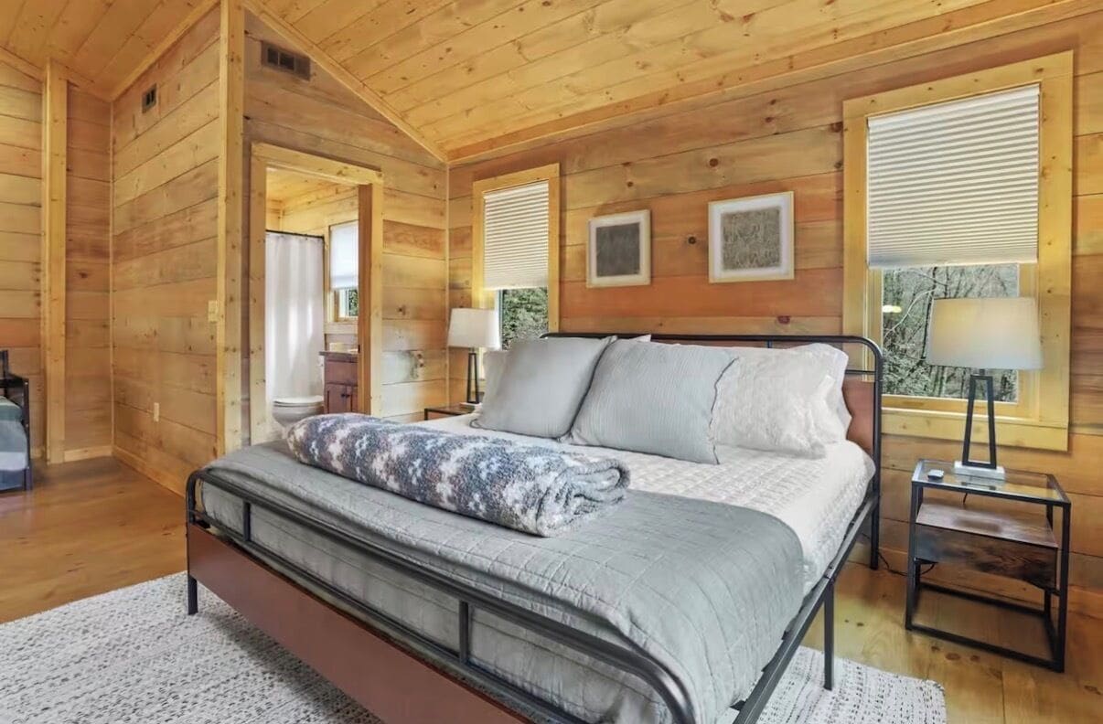 A wooden-paneled bedroom with a bed, bedside tables, and a window with blinds.
