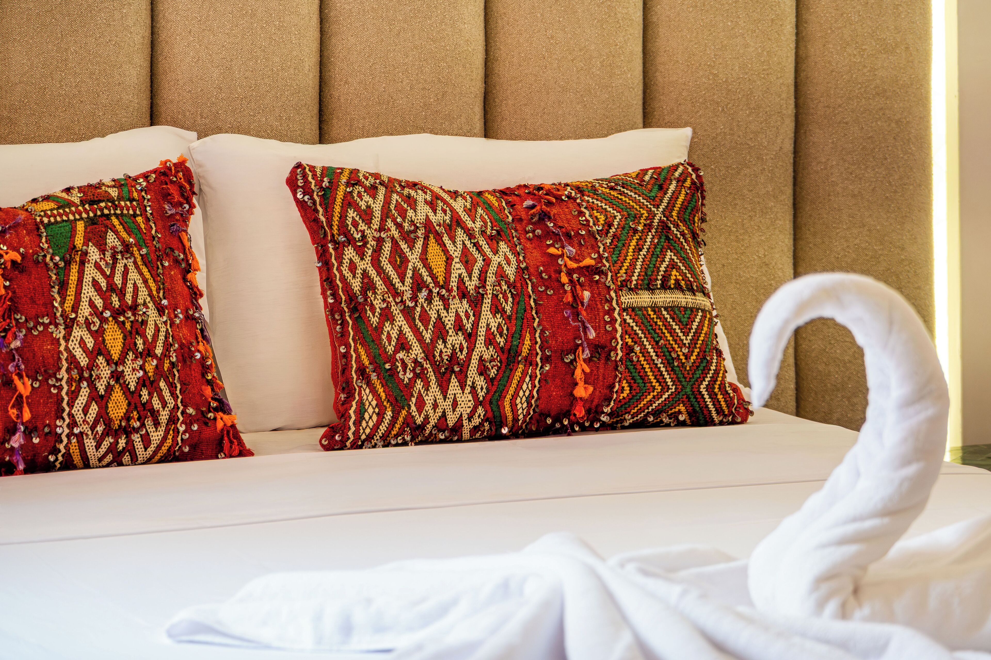 A hotel bed with two decorative pillows and a white towel.