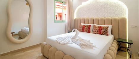 Habitación de hotel con una cama grande, un espejo redondo, un panel decorativo en la pared y una mesita.