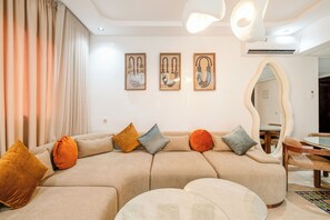 En moderne stue med en hjørnesofa, et rundt sofabord og et spiseområde med et glasbord og stole.