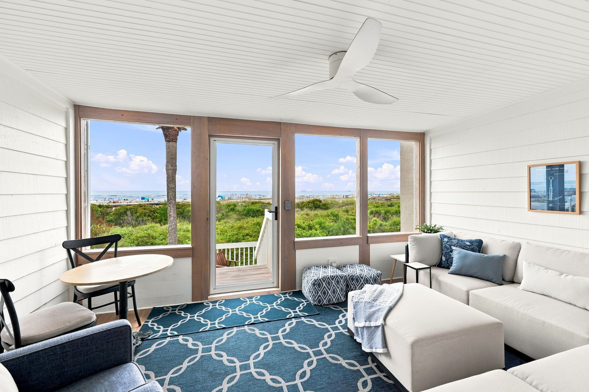 Ein Zimmer mit Blick auf den Strand, inklusive Deckenventilator, Sofa, Couchtisch und Sessel.
