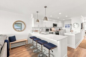 A modern kitchen with white cabinetry, a central island with bar stools, and pendant lighting. - Modern Oceanfront Beach Club Villa *Unit 4* in Wild Dunes w/Community Pool! Screen Porch!! (Isle Of Palms)
