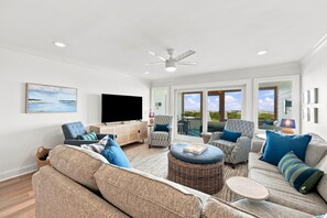 A spacious living room with a flat-screen TV, comfortable seating, a ceiling fan, and large windows offering a view. - Modern Oceanfront Beach Club Villa *Unit 4* in Wild Dunes w/Community Pool! Screen Porch!! (Isle Of Palms)