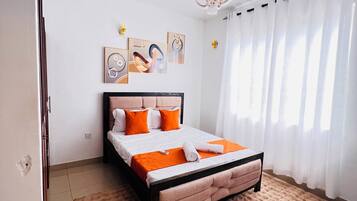 Ein Schlafzimmer mit Bett, Teppich, Vorhängen und Wandbildern.