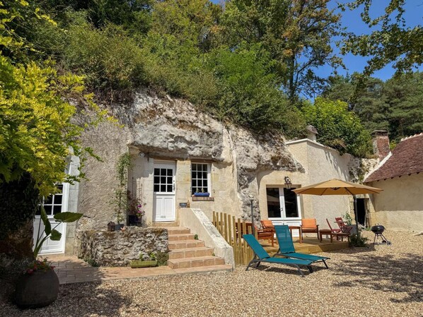 Une maison en pierre avec une porte d’entrée, des marches menant à un porche, un espace salon extérieur et un barbecue.