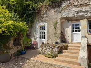 Un bâtiment rustique en pierre, doté d’un petit jardin, d’un banc en bois et d’un escalier menant à une porte.