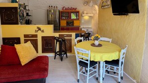 A compact kitchen with a dining area, a red sofa, and a TV mounted on the wall. - Unique troglodyte cave - 4 guests (Nazelles-Négron)