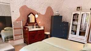 A bedroom with a bed, a vanity with a mirror, a cabinet with books, and a dresser. - Unique troglodyte cave - 4 guests (Nazelles-Négron)