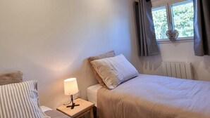 Quarto com uma cama, mesa de cabeceira com luminária, janela com cortinas e radiador.