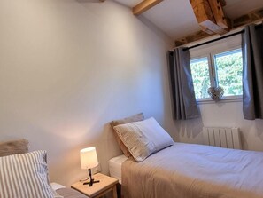 Ein Schlafzimmer mit einem Bett, einem Nachttisch mit Lampe, einem Fenster mit Vorhängen und einer Heizung.