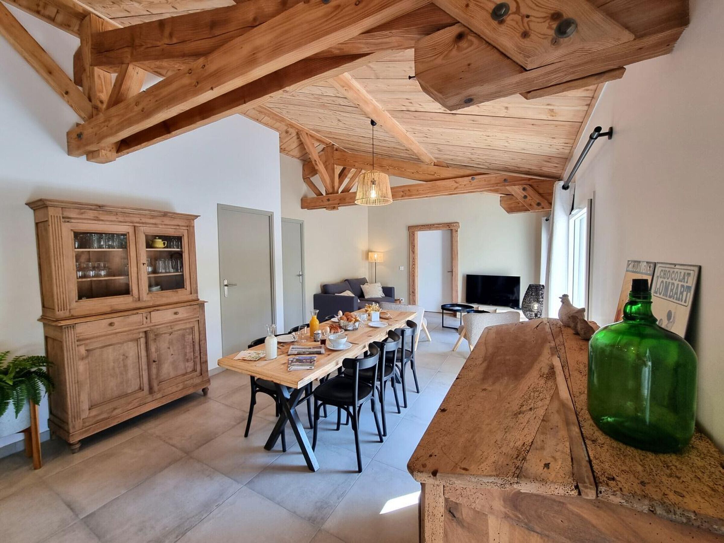 Ein geräumiger Wohnbereich mit Holzboden, einem Esstisch mit Stühlen, einer Vitrine und einem Fernseher im Hintergrund.