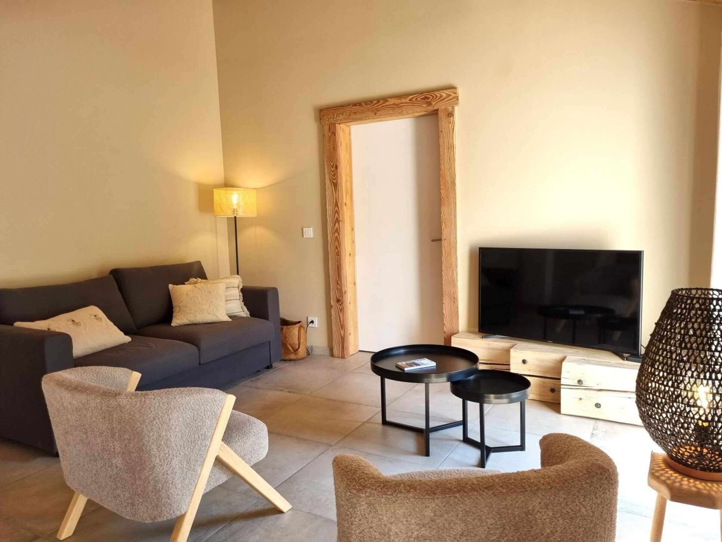 Una sala de estar moderna con un sofá, dos sillones, una mesa de centro, un televisor y una lámpara.