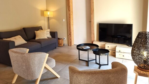 Uma sala de estar moderna com um sofá, duas poltronas, uma mesa de centro, uma televisão e um abajur.