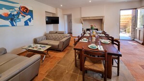 A living room with a sofa, a coffee table, and a TV mounted on the wall. There is a dining area with a long table set for six, surrounded by chairs. - House with pool and AC - 12 guests (CHANDON)