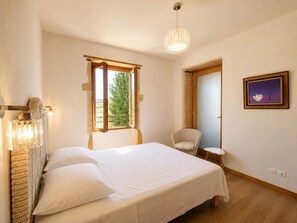 Ein Schlafzimmer mit einem Bett, einem Sessel, einem kleinen Tisch, einem Fenster und einem Bild an der Wand.