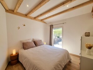 Ein Schlafzimmer mit einem Bett, zwei Nachttischlampen, einer Holzbalkendecke und Blick ins Freie.