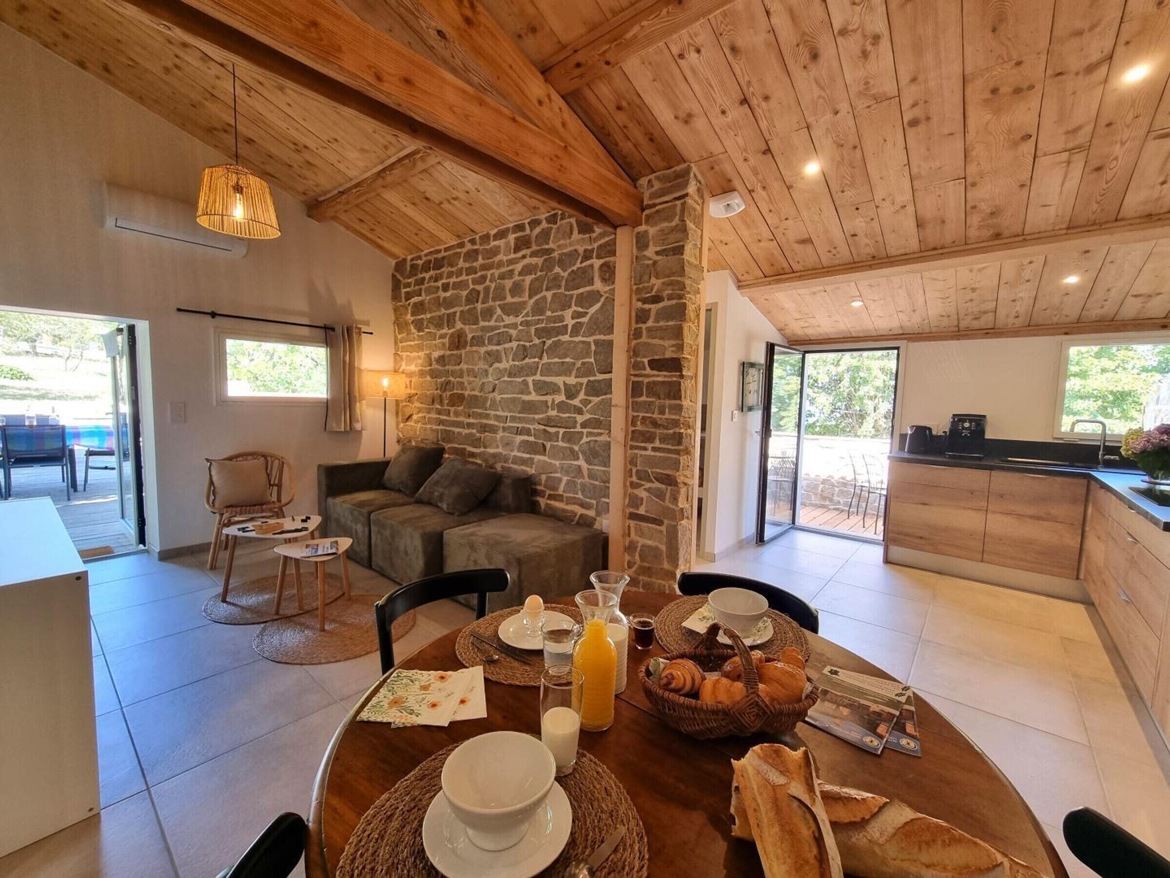 Una habitación acogedora con pared de piedra, techo de madera, una mesa de comedor dispuesta para el desayuno y vistas al exterior.